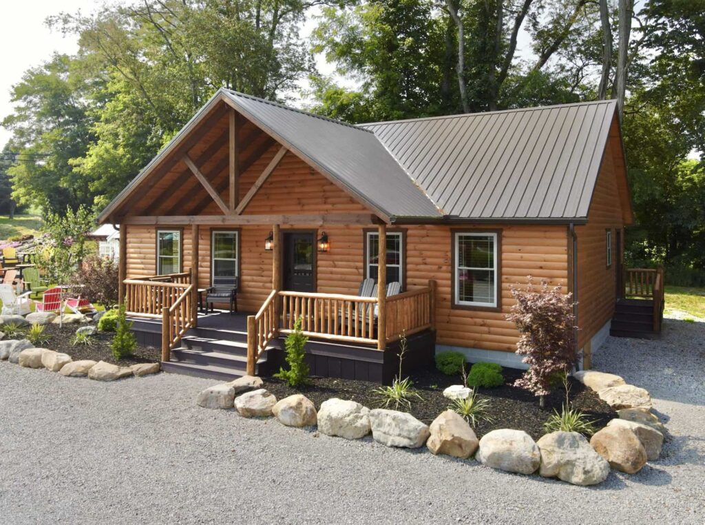 Log cabin home from Salem Structures featuring natural log siding, covered front porch, metal roof, and landscaped stone border on display lot.