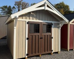 Beige craftsman-style storage shed from Salem Structures with brown double doors, board-and-batten siding, and decorative white trim.