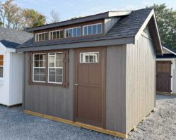 Brown and tan garden shed from Salem Structures featuring transom windows, craftsman trim, single entry door, and upgraded roofline on gravel display lot.